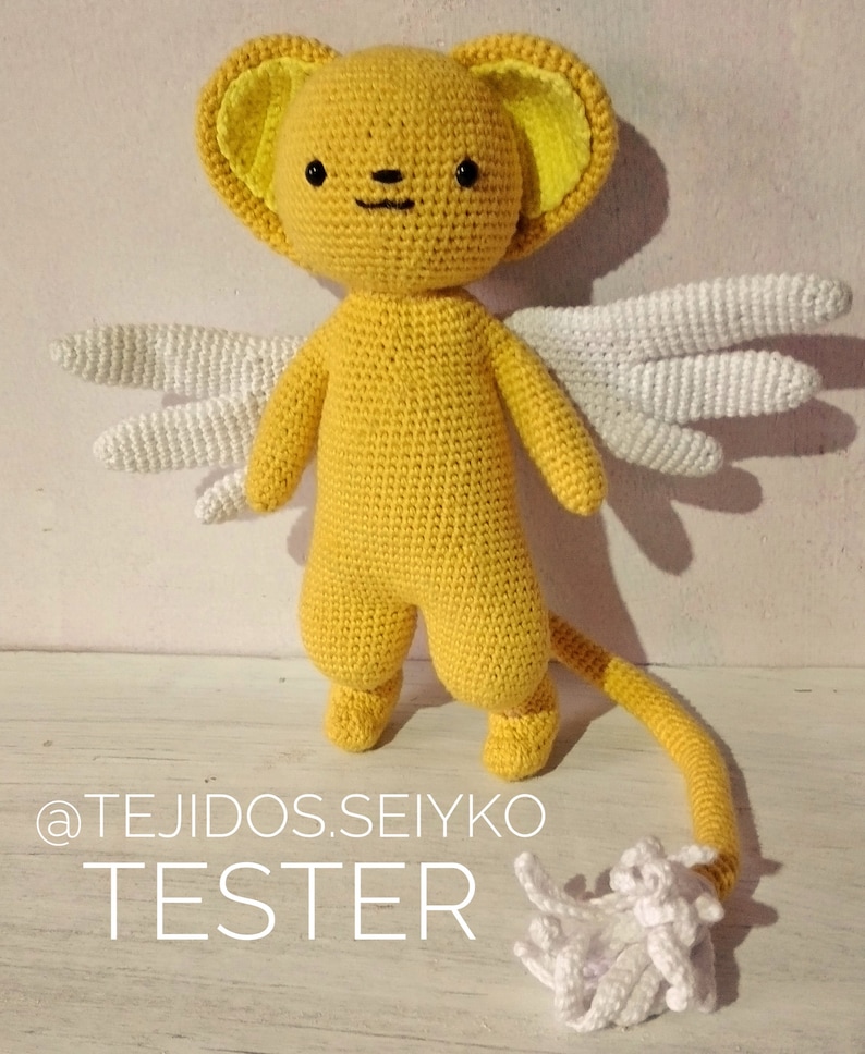 Puede incluir: Un juguete de peluche amarillo tejido a crochet con alas blancas y cola. El juguete tiene una cabeza redonda con ojos negros y una nariz negra. El juguete est&aacute; de pie sobre una superficie de madera. El texto "@TEJIDOS.SEIYKO TESTER" es visible en la imagen.