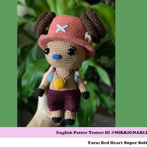 Puede incluir: Juguete de peluche tejido a crochet de un personaje que lleva un sombrero rojo y blanco con una cruz. El juguete es marr&oacute;n, con la nariz azul y los ojos marrones. El juguete lleva una camisa granate y un collar amarillo. El juguete lleva una mochila azul y blanca. El texto "English Pattern Tester: IG @NIKKIGNARLEA Yarn: Red Heart Super Soft" est&aacute; en la parte inferior de la imagen.
