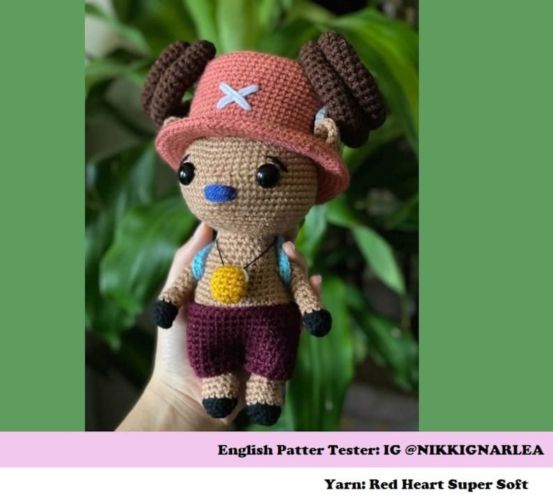 Puede incluir: Juguete de peluche tejido a crochet de un personaje que lleva un sombrero rojo y blanco con una cruz. El juguete es marr&oacute;n, con la nariz azul y los ojos marrones. El juguete lleva una camisa granate y un collar amarillo. El juguete lleva una mochila azul y blanca. El texto "English Pattern Tester: IG @NIKKIGNARLEA Yarn: Red Heart Super Soft" est&aacute; en la parte inferior de la imagen.