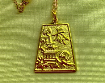 May include: A gold necklace with a pendant featuring a detailed, embossed design of a pagoda with stylized trees and flowers. The pendant is rectangular and has a slightly textured surface.