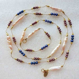 May include: A long gold chain necklace with baroque pearls, dark blue beads, and burgundy beads.
