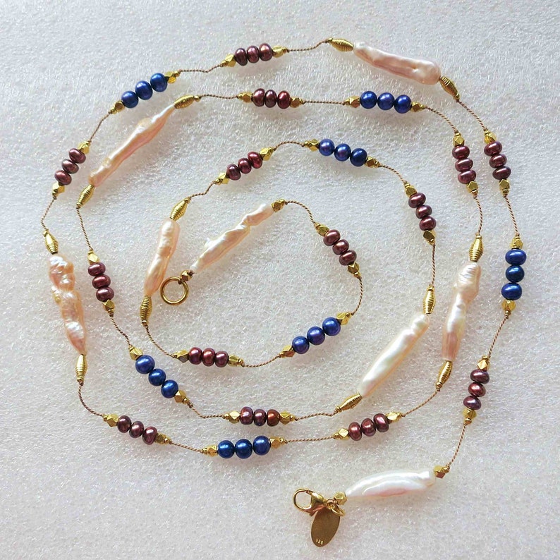 May include: A long gold chain necklace with baroque pearls, dark blue beads, and burgundy beads.