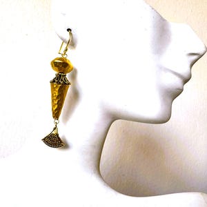 May include: Gold-toned dangle earrings with a textured, cone-shaped pendant and a fan-shaped charm. The earrings feature a hammered texture and a decorative top, showcasing an elegant, vintage design. The earrings are displayed on a white mannequin.