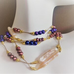 May include: A multi-strand necklace with purple, brown, and white pearls. The necklace is made with gold-colored beads and wire.