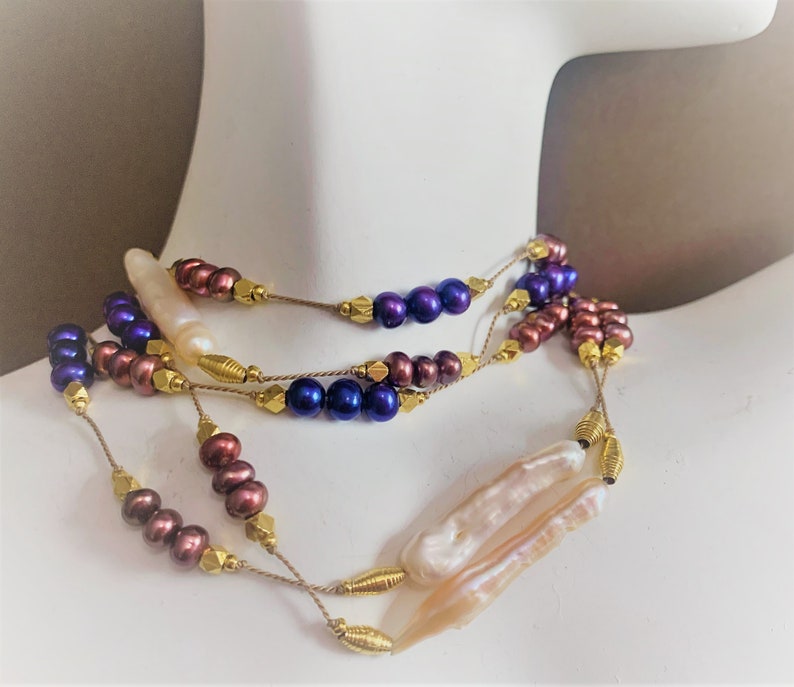 May include: A multi-strand necklace with purple, brown, and white pearls. The necklace is made with gold-colored beads and wire.