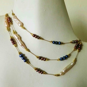 May include: A multi-strand necklace with gold chain and pearls. The necklace features three strands of pearls in different colors: white, blue, and brown.