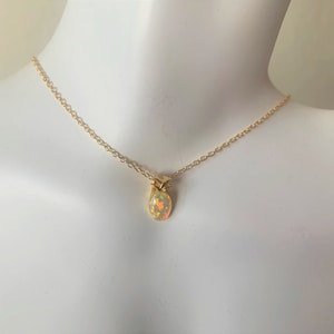 May include: A gold chain necklace with a small, oval-shaped opal pendant in the shape of a pineapple.