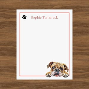 Puede incluir: Papelería blanca con borde rojo e ilustración en acuarela de un bulldog. El texto "Sophie Tamarack" está impreso en rojo, con una huella de pata negra en la esquina superior izquierda.