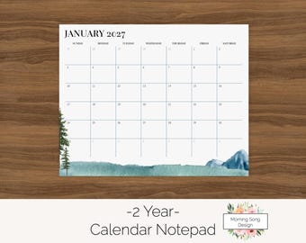 Può includere: Un blocco note calendario in carta bianca per gennaio 2027 con una griglia per i giorni della settimana. La parte inferiore presenta un'illustrazione ad acquerello di pini verdi e montagne blu. Il testo in basso recita 2 Year Calendar Notepad.