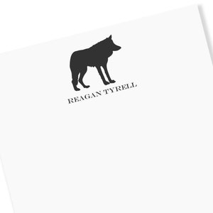May include: A white stationery sheet featuring a black silhouette of a wolf. The text "REAGAN TYRELL" is printed in black below the wolf image. The stationery has a clean, minimalist design.