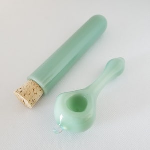 May include: A light green glass pipe with a rounded bowl and a long, slender stem. The pipe is paired with a matching light green glass tube with a cork stopper.