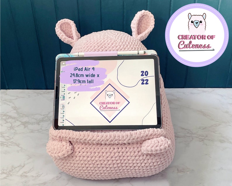 May include: A pink crocheted llama-shaped stand for an iPad Air 4. The stand is 24.8 inches wide and 17.9 inches tall. The iPad is displaying a digital planner with the text "CREATOR OF Cuteness" on the screen.