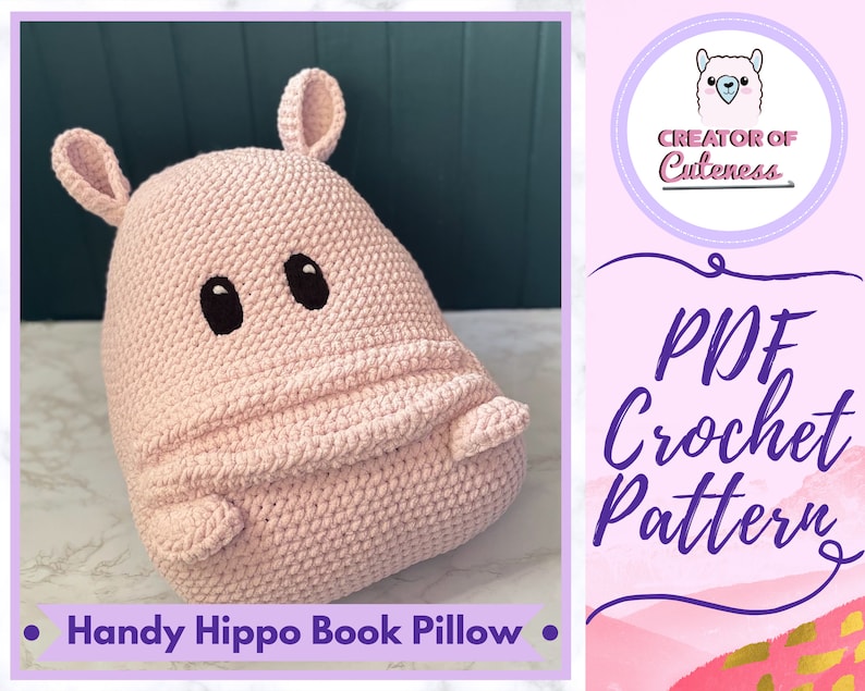 May include: A pink crocheted hippopotamus book pillow. The pillow has black eyes and a cute expression. The text "Handy Hippo Book Pillow" is at the bottom of the image. The image also includes a pink and gold background with the text "PDF Crochet Pattern" and a logo that says "Creator of Cuteness".