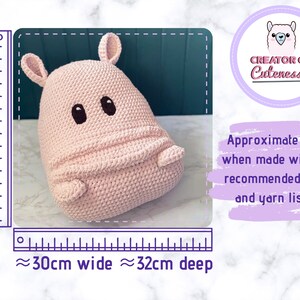 May include: A pink crocheted hippopotamus plush toy with black eyes and a stitched smile. The toy is approximately 35 cm tall, 30 cm wide, and 32 cm deep. The image includes a ruler for size reference.