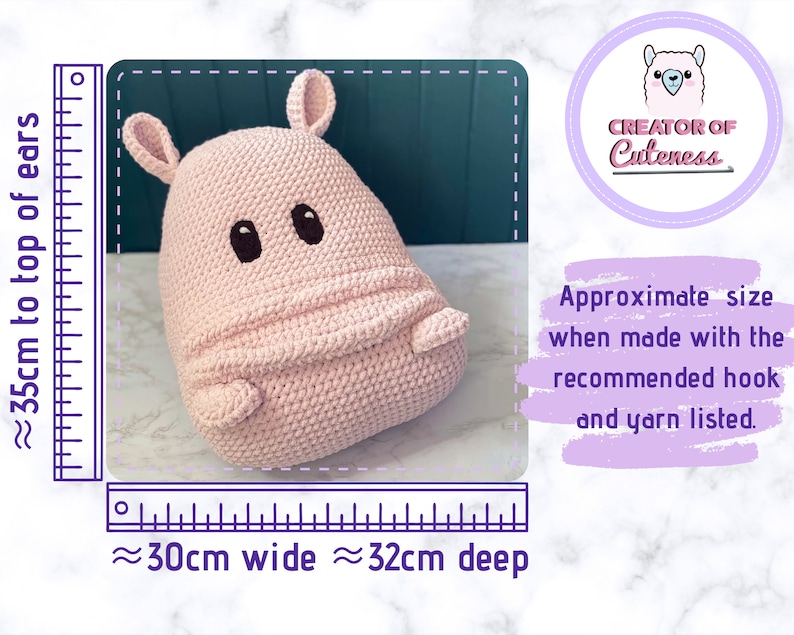 May include: A pink crocheted hippopotamus plush toy with black eyes and a stitched smile. The toy is approximately 35 cm tall, 30 cm wide, and 32 cm deep. The image includes a ruler for size reference.