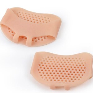 May include: Two beige silicone metatarsal pads with a honeycomb design. Each pad has a loop for the second toe and a small section for the third and fourth toes. The pads are designed to cushion the ball of the foot.