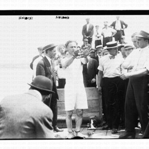 May include: A black and white photograph of a group of people, including a man in a white shirt and a hat, performing a magic trick. The man in the white shirt is holding his hands up in the air, and the other people are watching with interest. The photo is labelled "HOUDINI" at the top.