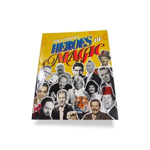 Puede incluir: Un libro amarillo titulado John Fisher's Heroes of Magic que presenta un collage de retratos en blanco y negro de varios magos y un tigre en la portada. El título está impreso en letras grandes azules y rojas sobre el fondo amarillo.