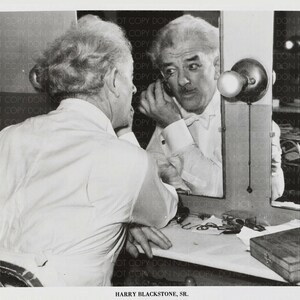 May include: A black and white photograph of a man in a white shirt adjusting his collar while looking in a mirror. The man is standing in front of a dressing table with a lamp and a small box on it. The text "HARRY BLACKSTONE, SR." is printed below the image.