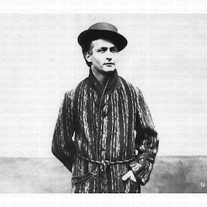 May include: A black and white photograph of a man wearing a striped dressing gown and a black fedora. He is standing with his hands in his pockets and looking at the camera.