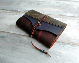 May include: A brown leather journal with a blue and green leather flap. The journal is tied closed with a brown leather strap and has a brown leather tassel with blue and green beads.
