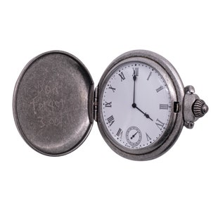 May include: A silver pocket watch with Roman numeral markings on the face. The watch is open and the inside of the case has the inscription "Don't forget 3/25/11".