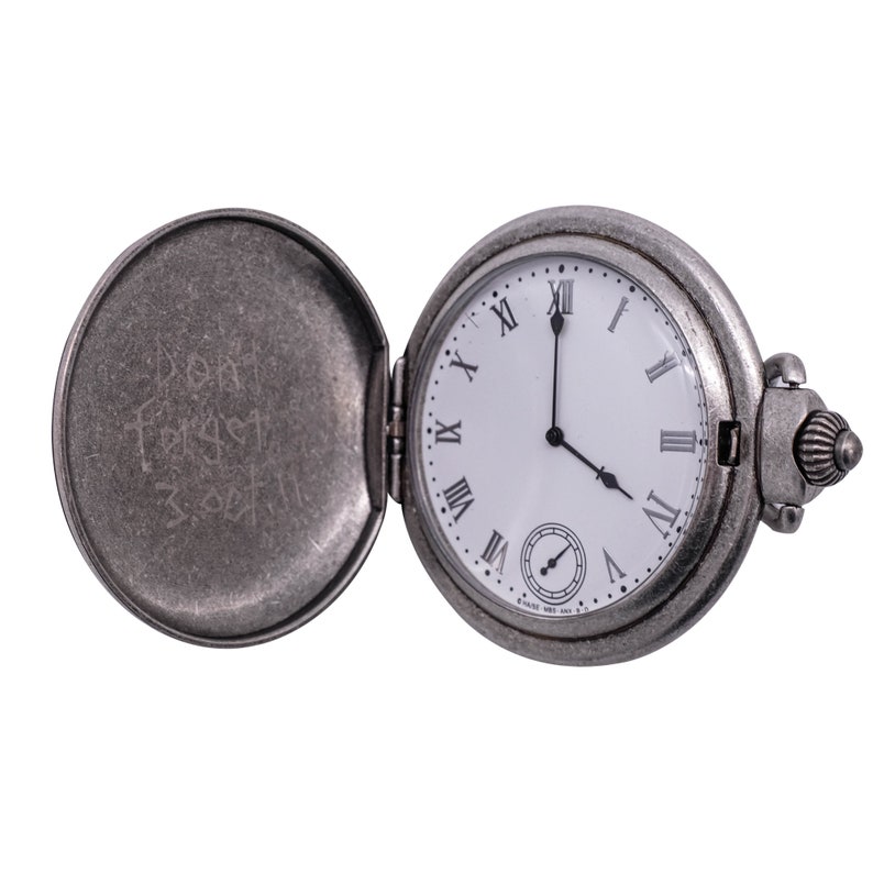 May include: A silver pocket watch with Roman numeral markings on the face. The watch is open and the inside of the case has the inscription "Don't forget 3/25/11".