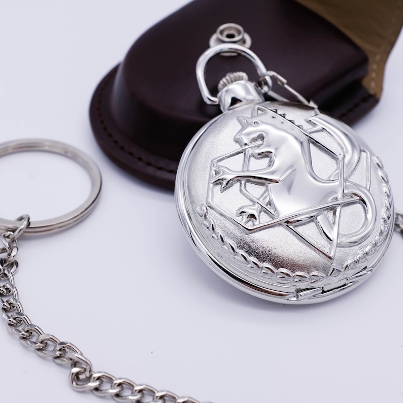 May include: A silver pocket watch with a chain and a leather case. The watch face features a lion emblem.