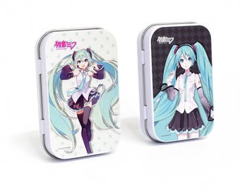 以下が含まれることがあります： 青い髪のアニメキャラクターの画像が描かれた白い金属製の缶が2つ。キャラクターは白いシャツ、黒いスカート、黒い太ももまであるハイソックスを着用しています。缶には「初音ミク」と書いてあります。