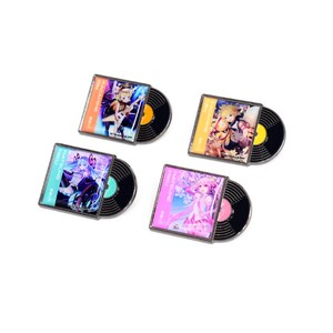 Può includere: Quattro spille smaltate a forma di dischi in vinile in miniatura. Ogni spilla presenta un design colorato della copertina dell'album con testo giapponese e un disco nero con un centro giallo. Le spille sono su uno sfondo bianco.