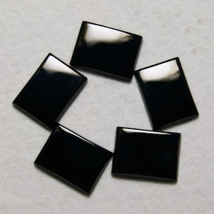 May include: Five glossy, rectangular black stones arranged in a circular pattern. Each stone has a polished, reflective surface, and they are set against a light gray background. The stones appear to be of uniform size and shape.