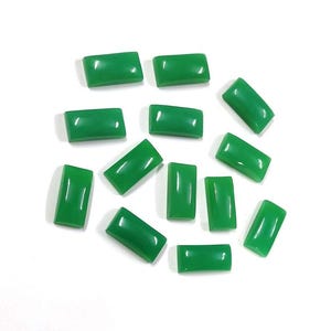 May include: A selection of rectangular, polished green gemstones. The stones are a vibrant, solid green colour and have a smooth, glossy surface. They are scattered on a white background, showcasing their shape and colour.