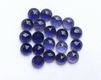 May include: A collection of faceted, round gemstones in varying shades of deep blue and purple. The gemstones are arranged on a white surface, showcasing their geometric cuts and reflective surfaces. The overall effect is one of elegance and luxury.
