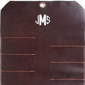 May include: A brown leather tool roll with a monogrammed "JMS" in white. The roll has eight stitched slots for holding tools.
