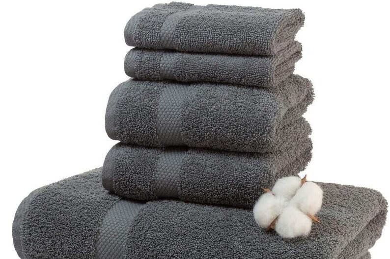 May include: A stack of six charcoal gray bath towels with a textured stripe design. A sprig of white cotton is placed on top of the towels. The towels are soft and fluffy, perfect for a bathroom.
