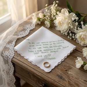 K&ouml;nnte beinhalten: Ein wei&szlig;es quadratisches Taschentuch mit gewelltem Rand und gr&uuml;ner Stickerei mit dem Text: Dad, To dry your tears as you have always dried mine. Thank you for walking by my side today and everyday. Today a bride, tomorrow a wife, forever your favorite daughter. I love you - Maddie. Ein goldener Ring liegt auf dem Stoff.