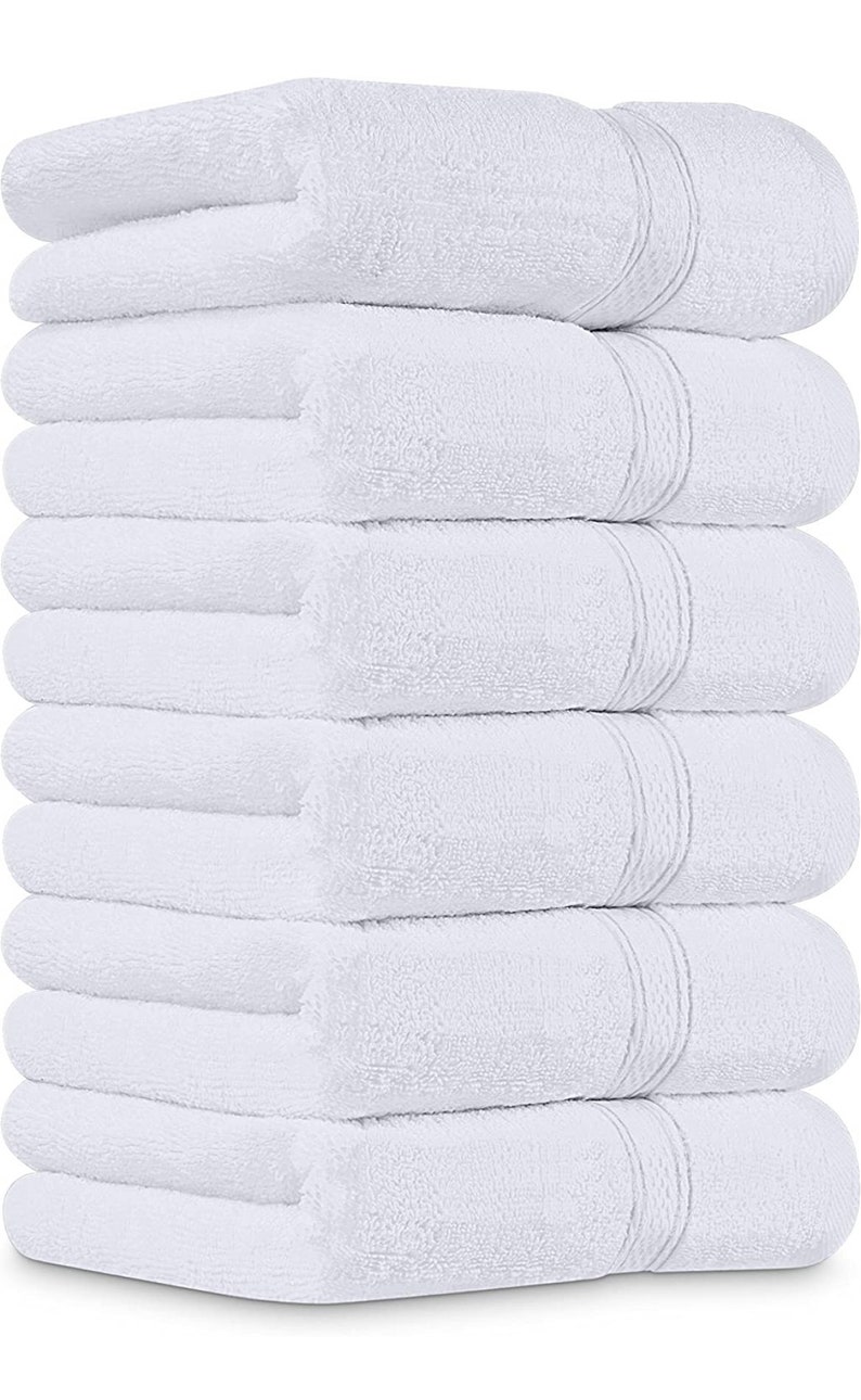 May include: A stack of eight white bath towels. Each towel is folded and has a textured surface. The towels are neatly arranged, with the folded edges aligned, creating a clean and organized appearance. The towels are a solid white color.