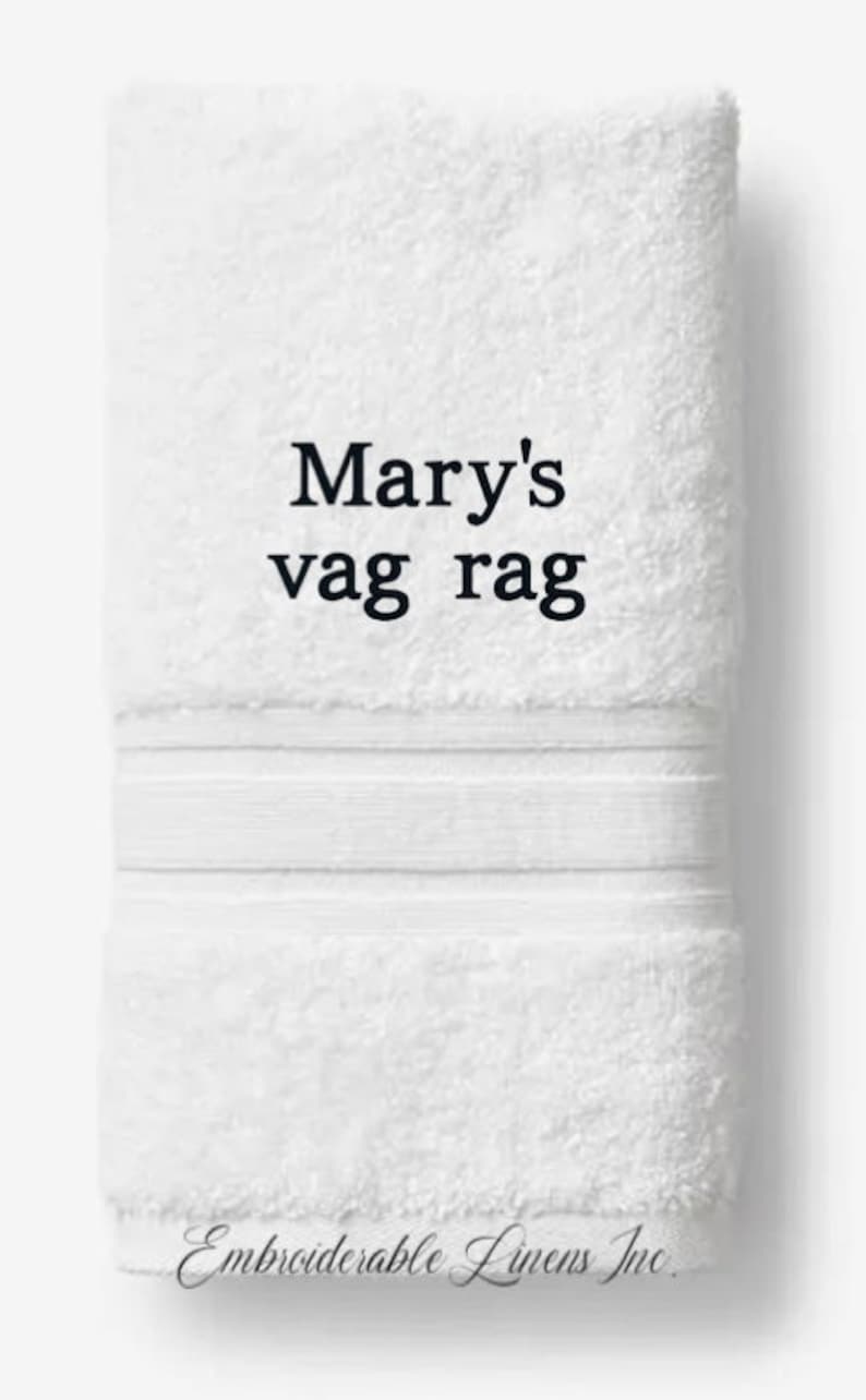 May include: White, rectangular towel with the text "Mary's vag rag" in black. The towel has a textured surface and a decorative band. The words "Embroiderable Linens Inc" are at the bottom.