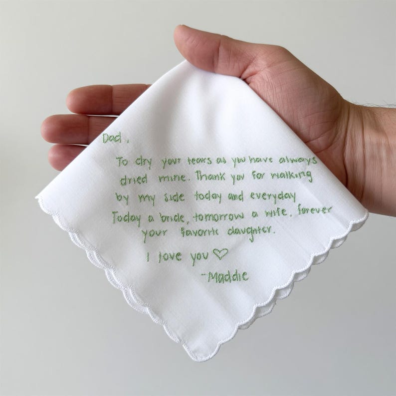 K&ouml;nnte beinhalten: Ein wei&szlig;es Taschentuch mit gewelltem Rand und gr&uuml;ner Stickerei mit dem Text: Dad, To dry your tears as you have always dried mine. Thank you for walking by my side today and everyday. Today a bride, tomorrow a wife, forever your favorite daughter. I love you -Maddie.