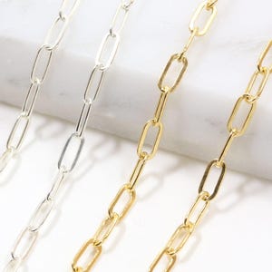 May include: Two delicate paperclip chains, one in a polished silver tone and one in a bright gold tone. Each chain features elongated, rectangular links connected in a continuous, uniform pattern, showcasing a clean and simple metallic design.