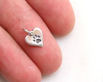 May include: Silver heart charm with a paw print design. The charm is small and delicate, perfect for adding a touch of personalization to jewelry.