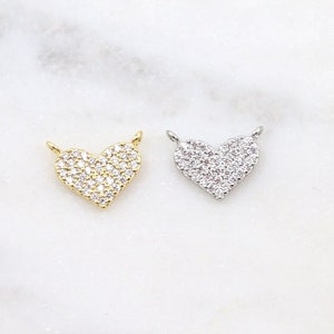 May include: Two heart-shaped pendants, one gold and one silver, both covered in small, clear cubic zirconia stones.