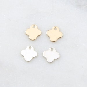 May include: Four metal charms in the shape of a four-leaf clover. Two charms are gold and two charms are silver.