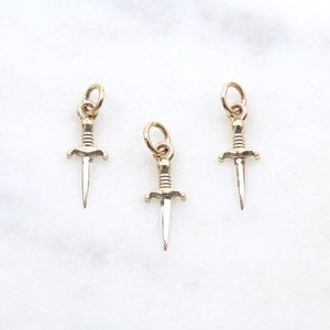 May include: Three gold dagger charms with a silver finish. The charms are on a white background.