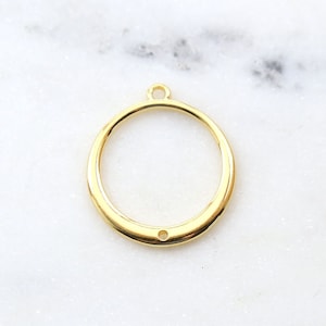 May include: Gold-toned metal circle pendant with a small hole at the top and a smaller hole at the bottom. The pendant is smooth and has a shiny finish.