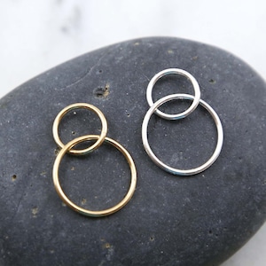 May include: Two pairs of hoop earrings, one gold and one silver, with a smaller hoop inside a larger hoop. The earrings are displayed on a gray stone.