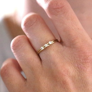 Op de afbeelding: Een delicate gouden ring met drie kleine, ronde diamanten in een rij.