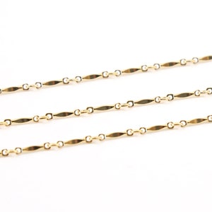 May include: Three gold chains with a flat, rectangular link design. The chains are laid out in parallel lines on a white background.