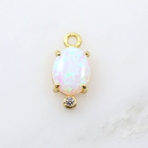 May include: Gold charm with a white oval opal gemstone and a small clear rhinestone.
