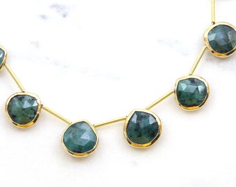 May include: A gold chain necklace with emerald green gemstone drops. The necklace is made of a delicate chain and features a series of teardrop-shaped gemstones.